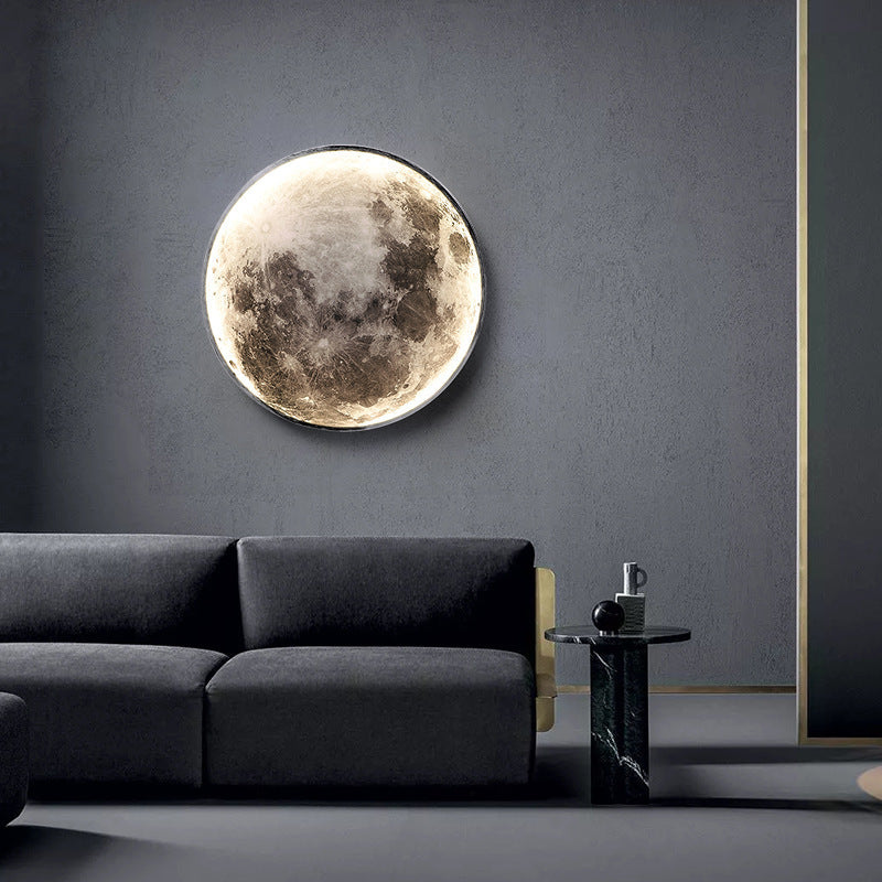 A realistic 3D textured moon mural wall lamp by CityLumi, glowing with a soft warm light on a dark gray microcement wall above a modern black sofa.